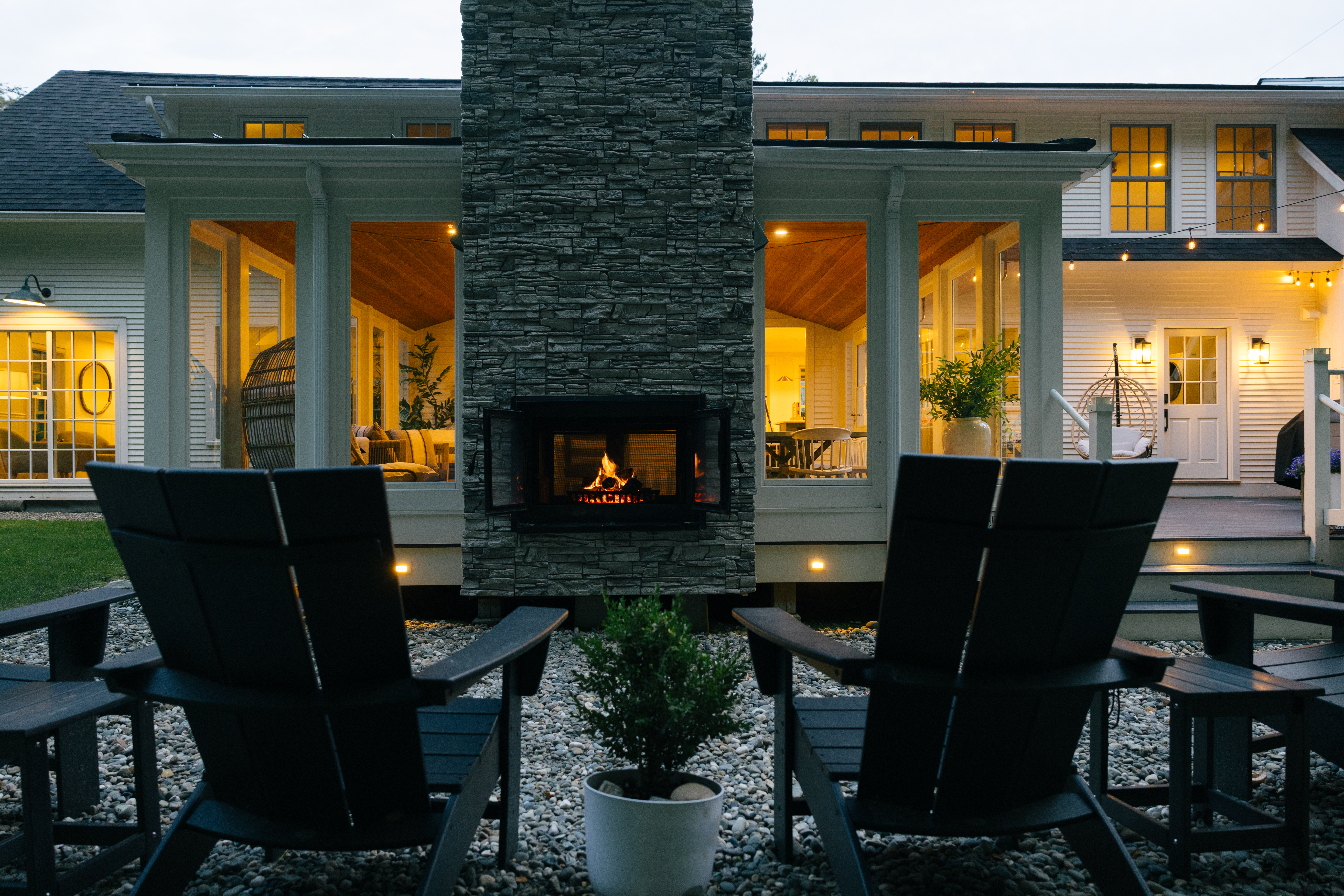 Stone outdoor fireplace with chairs on the patio at dusk